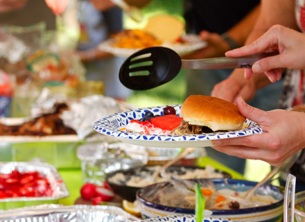 table with loads of BBQ with people putting food on plate and other people in background